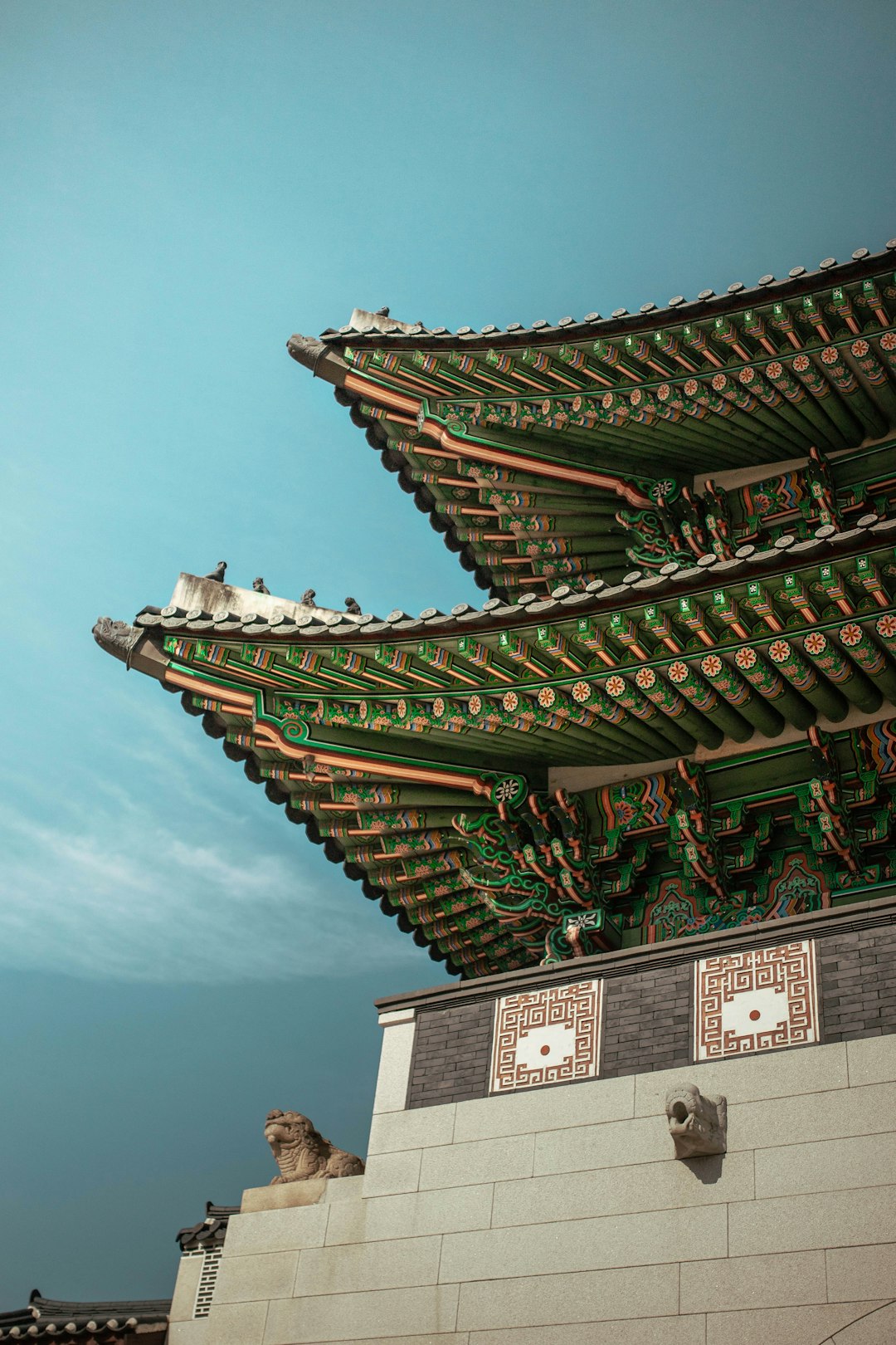 Ornate green and red eaves of a traditional Korean palace against a blue sky