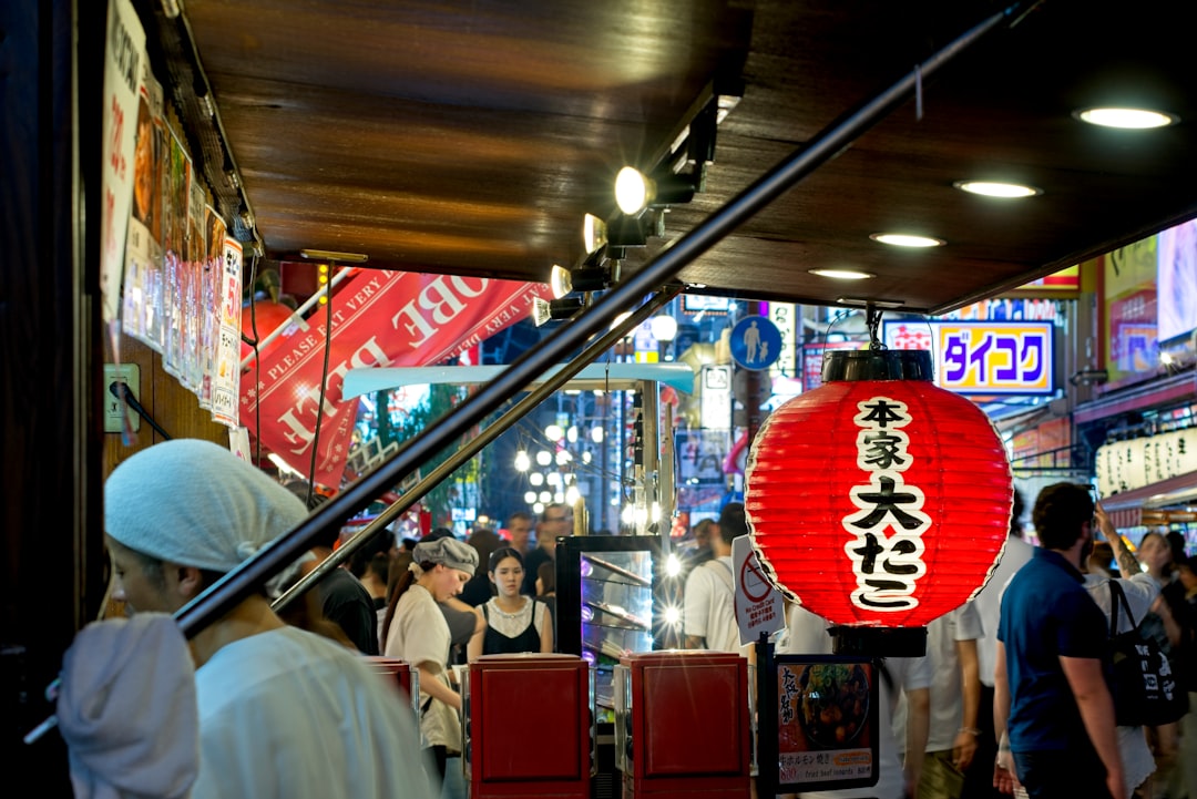 A red paper lantern hanging above a busy street food stall in Osaka
