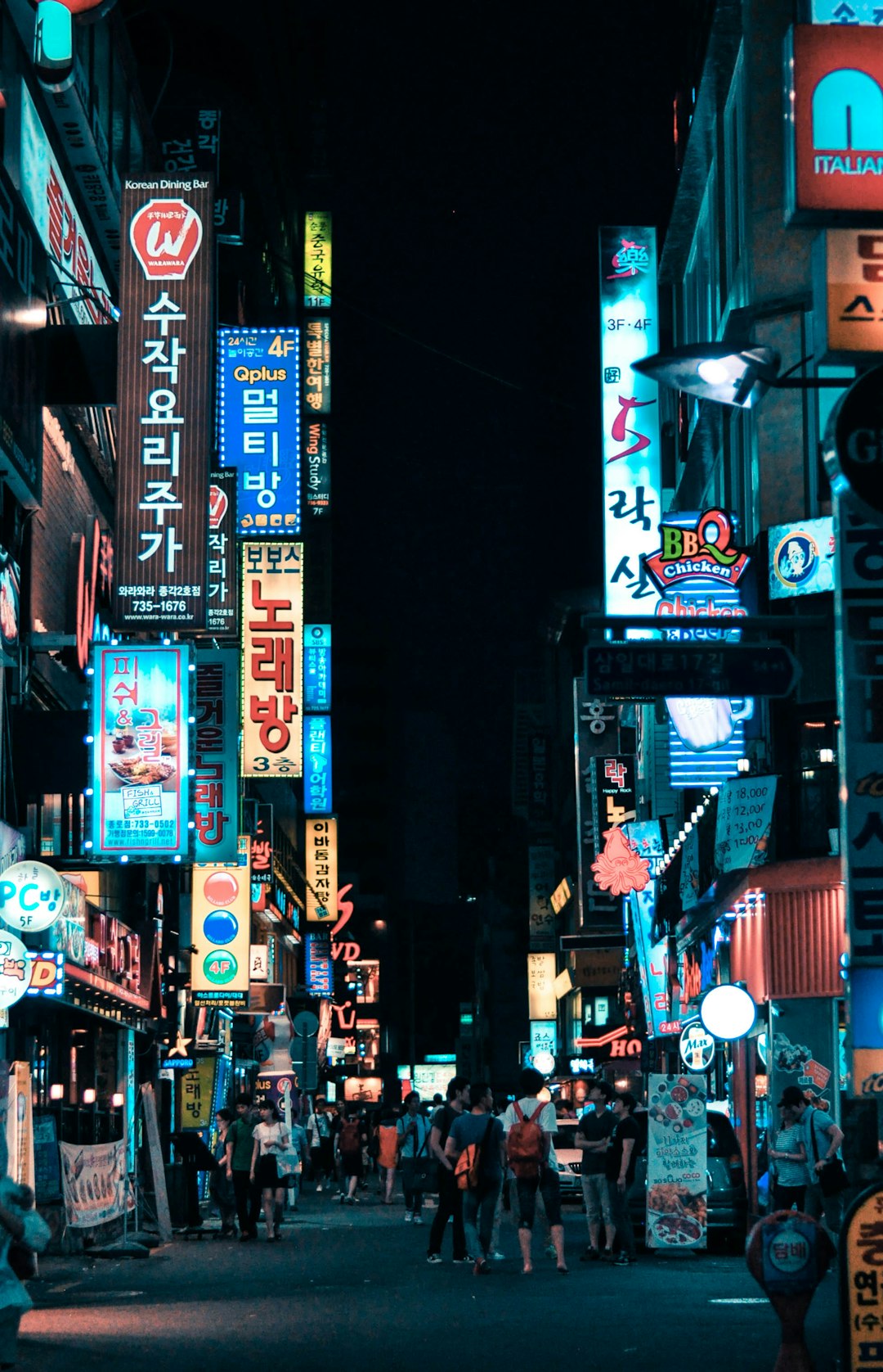 People walking down a narrow street in Seoul lined with glowing neon signs