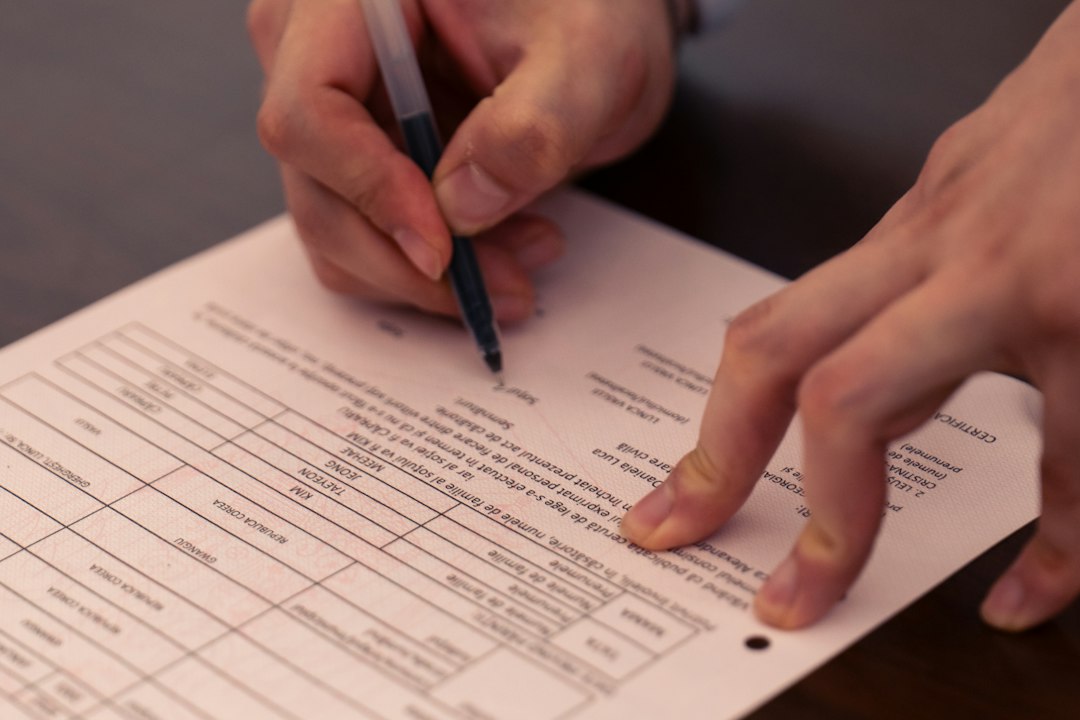 Hands holding a pen and signing a formal document on a dark surface